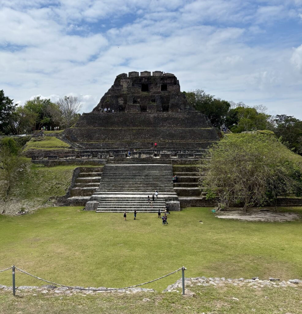 View of the ancient Mayan ruins of Xunantunich, featuring a large stone pyramid and a grassy area with visitors exploring.