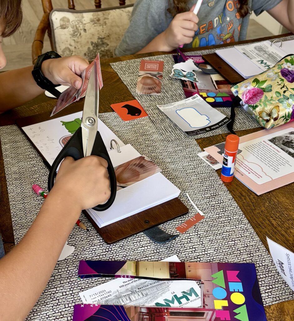 Children engaged in crafting scrapbooks, using scissors, glue sticks, and colorful papers on a table scattered with various art supplies.