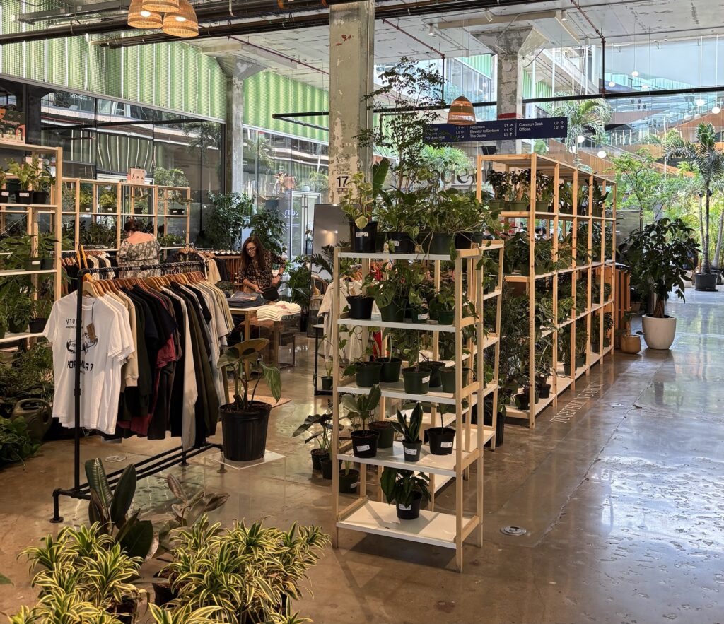 Interior view of a vibrant plant shop featuring shelves of potted plants and clothing racks. At the POST Houston.